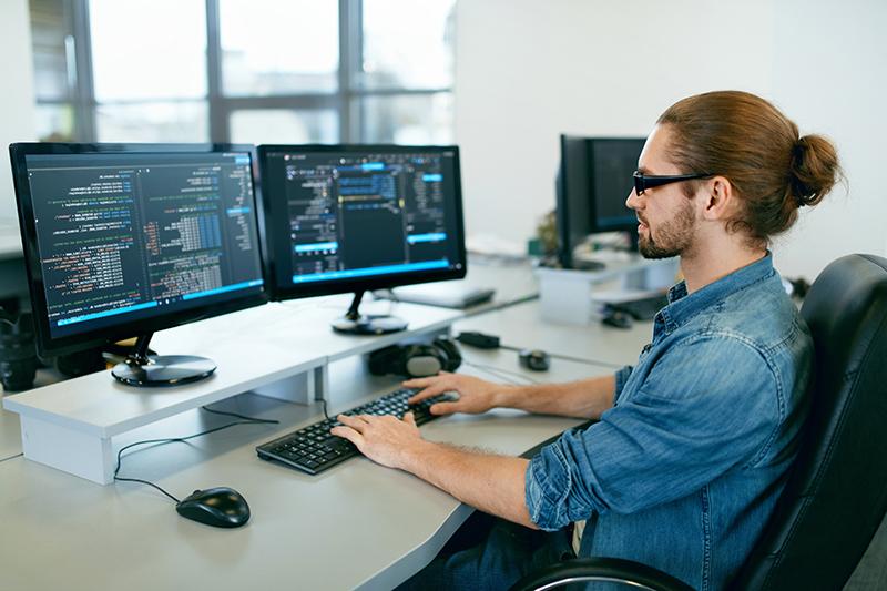 Programmazione. Uomo che lavora al computer in un ufficio informatico, seduto alla scrivania a scrivere codici. Programmatore che digita il codice di dati, lavorando al progetto nella società di sviluppo del software. Immagine di alta qualità.